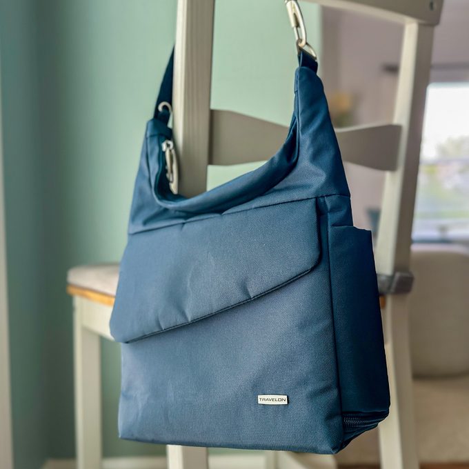A blue shoulder bag hangs on a chair in a softly lit room. The bag features a 