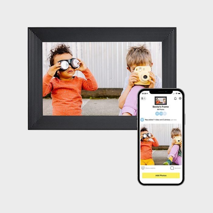 Children hold toy cameras; one has binoculars. They are outdoors against a corrugated wall. A smartphone shows the same image labeled 