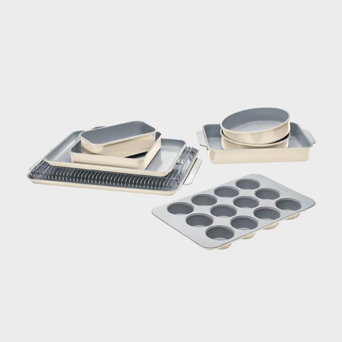 Baking pans and trays are arranged neatly on a neutral surface, including round and muffin trays, creating a kitchenware assortment.