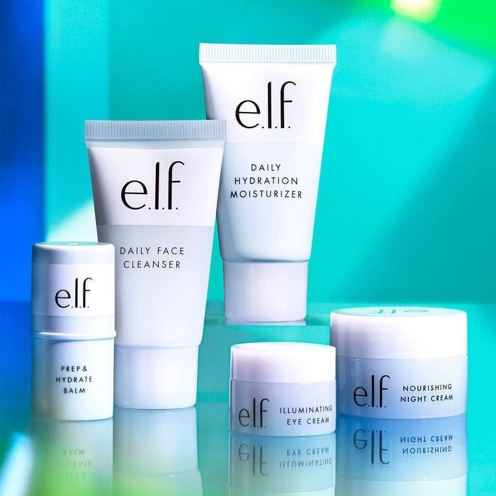 Skincare products stand arranged on a reflective surface with a vibrant blue-green gradient background. Text includes: 