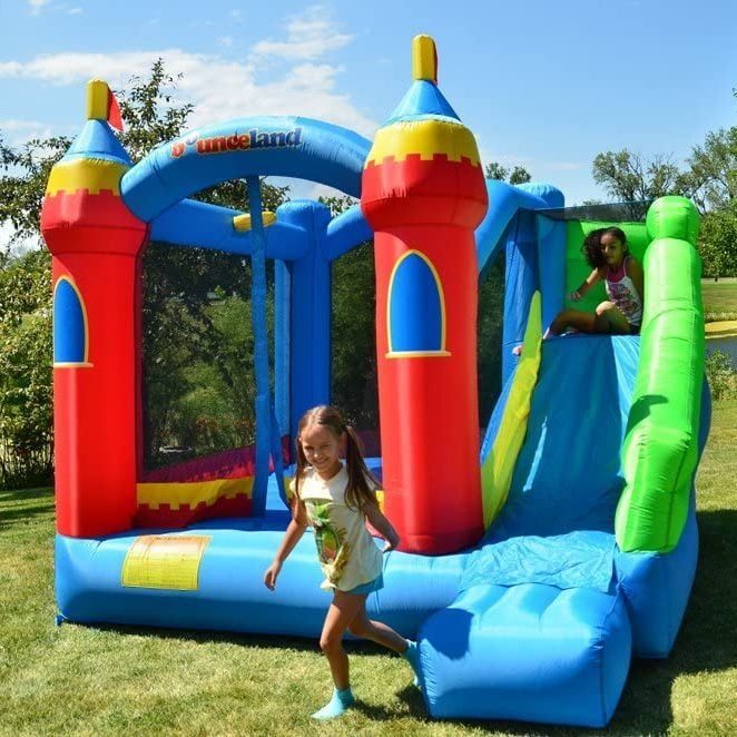 Inflatable castle with slide; a child slides while another runs on grass under a clear sky; text reads 