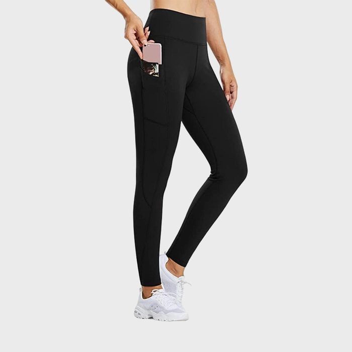 Leggings hold a phone in a side pocket; worn with white sneakers, shown against a plain gray background.