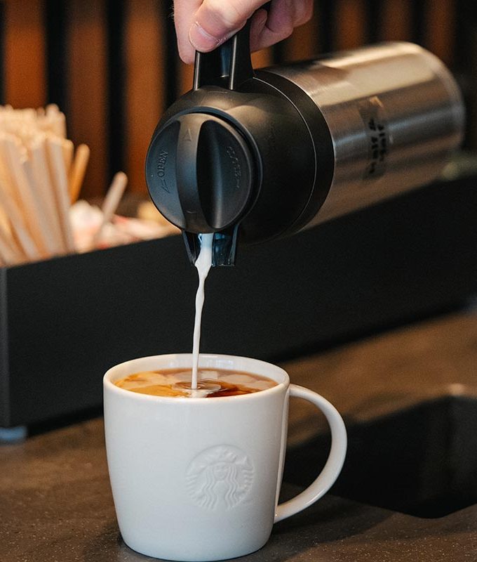 Milk is poured into a ceramic Starbucks mug at a condiment bar