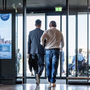 Two men exit through glass doors at an airport