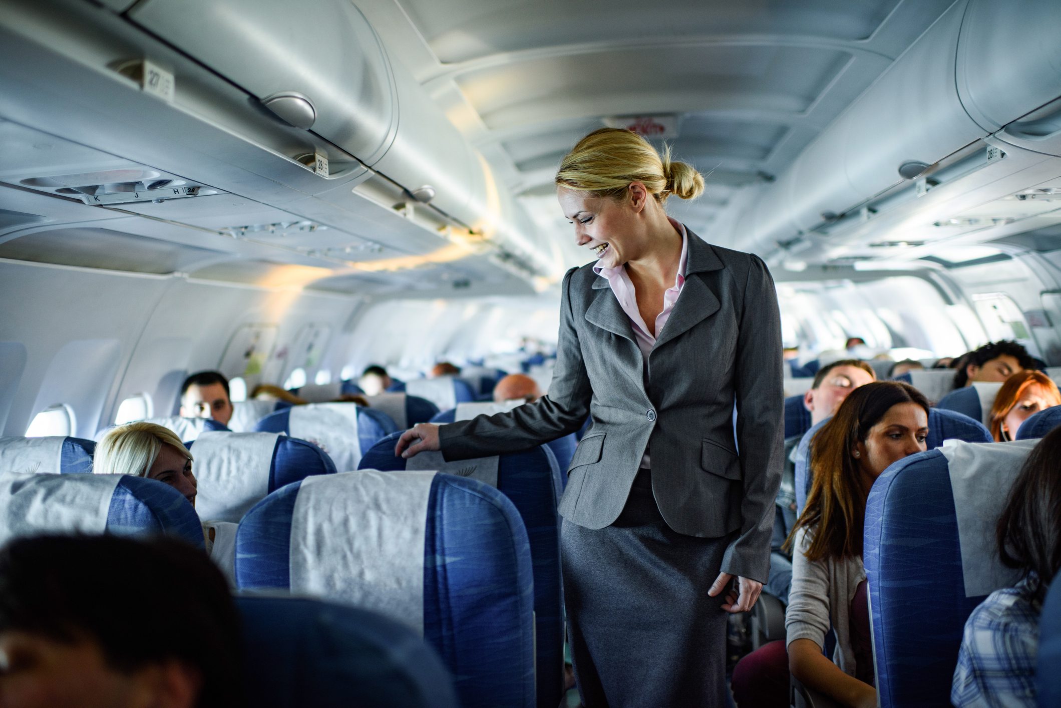 Happy female flight attendant talking to passenger in a plane.