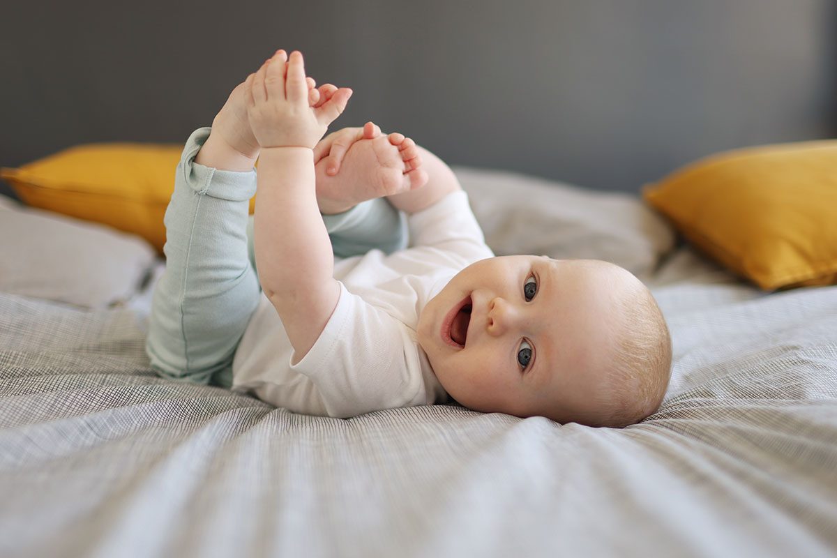 A 6 month old baby boy smiling, laying on a bed