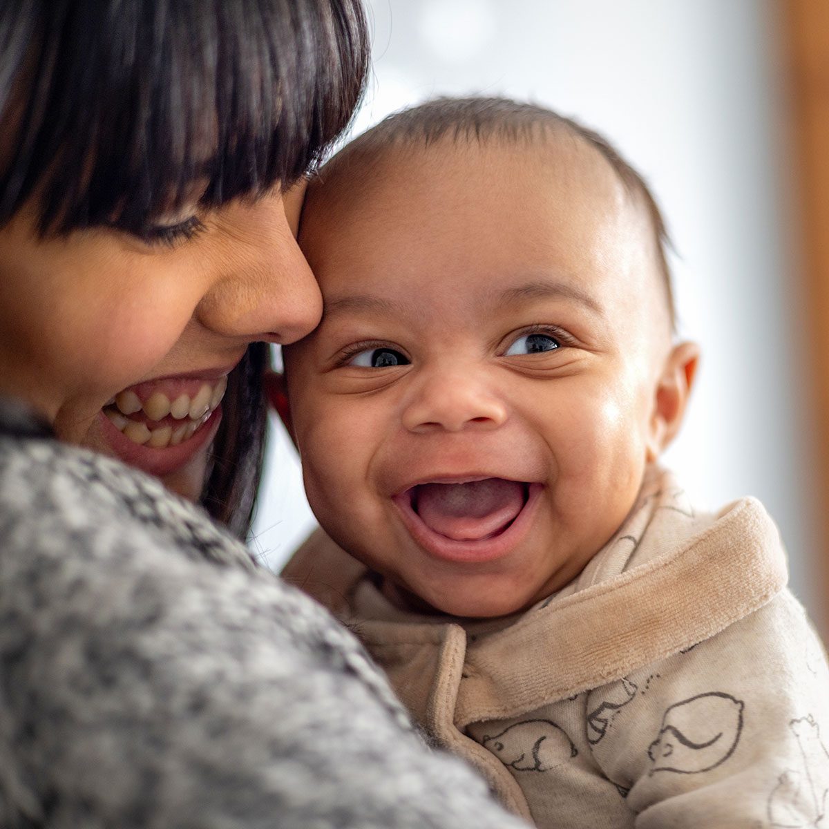 Close-up of a mother holding her baby boy near her face. The baby boy is laughing looking away