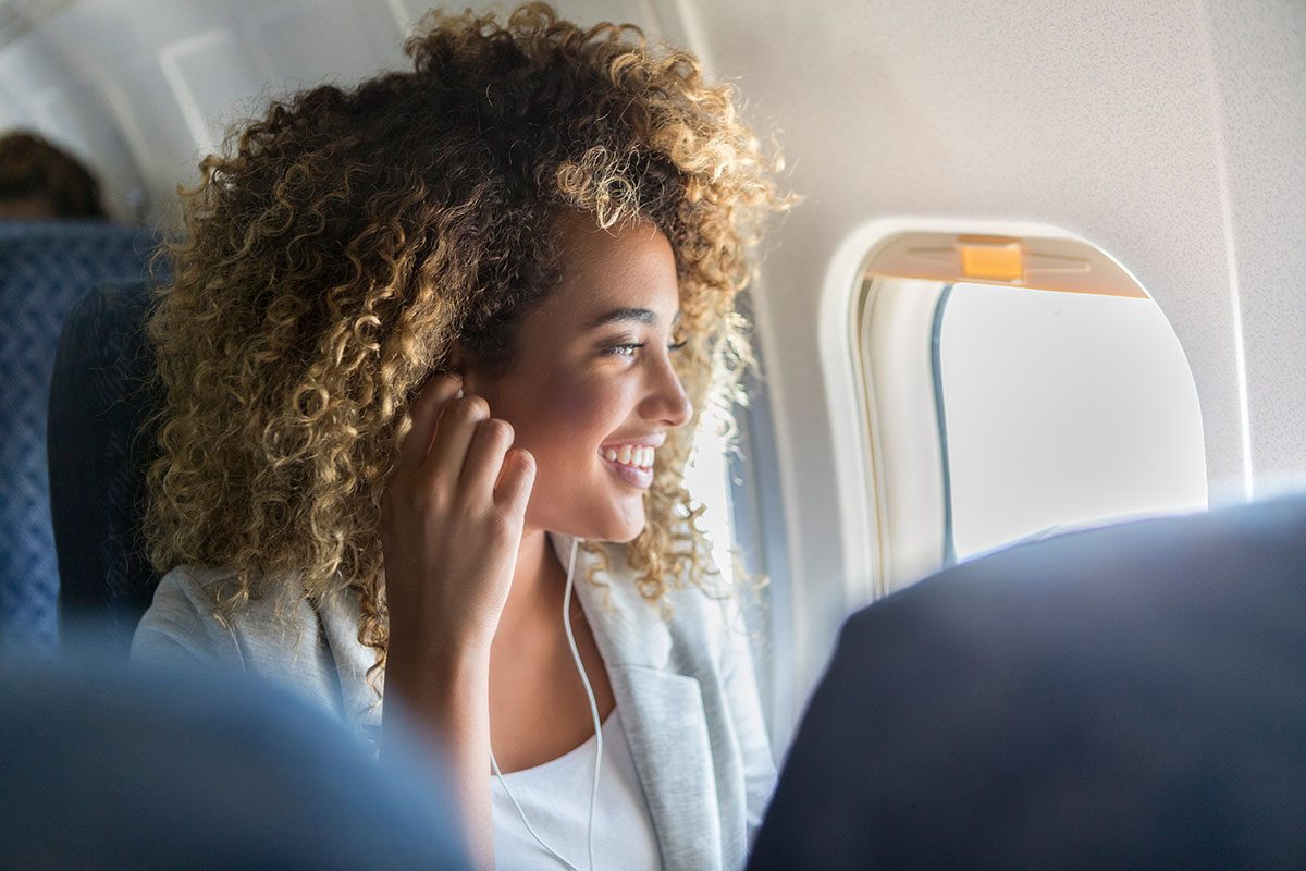 young woman wears earbuds to listen to music during a flight.